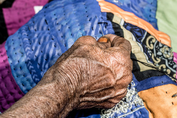 an old woman is stitching a traditional Asian blanket cause of high poverty ratio  