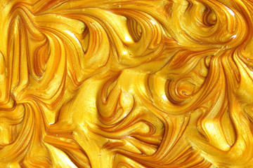 Close up liquid luxury gold metallic glitter paint swirls to make an abstract textured background