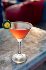 orange cocktail with a lime on a beach table top