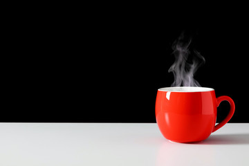 Steaming coffee cup on black background. Red сoffee cup with steam. Smoke from hot coffee. Front view, copy space