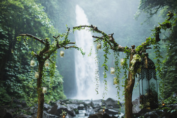 Wedding ceremony on huge waterfall Nung Nung in Bali, Indonesia jungle. Arch with dry wooden branches and green ivy. Unusual destination for wedding.