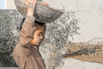 a very young orphan child is forced into child labor and working at a construction site and his expressions area full of pain  