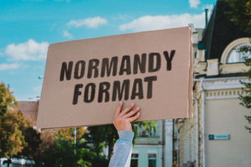 The phrase " Normandy Format " on a carton banner in men's hand. Human holds a cardboard with an inscription. Politics. War. Europe. Peace. Conflict