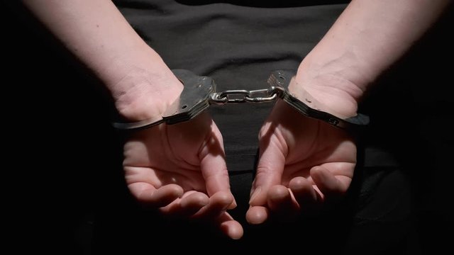 Handcuffs on hands of criminal behind his back on black background close-up.