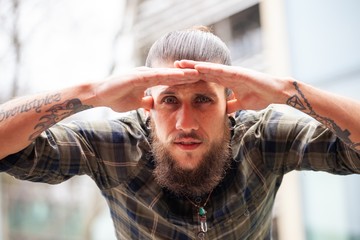 young man with beard and gauged pierced ears with looking with hand shielding sun
