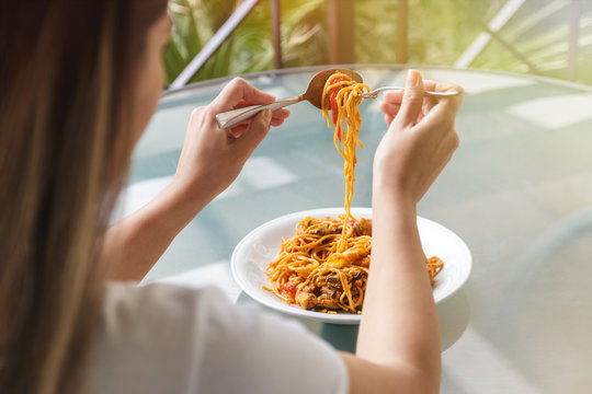 close up of woman eating spaghetti with fork and tablespoon