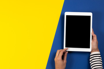 Female hands with digital tablet computer on navy blue and yellow background. Top view