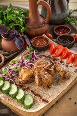 chicken shish kebab on lavash bread with red onion, tomato, cucumber and tomato sauce on wooden table