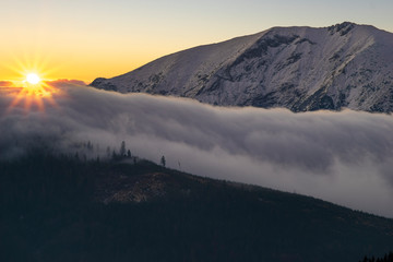 sunrise over the embankment from clouds overflowing over the tops of the mountains