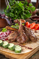 Grilled lamb ribs on lavash bread with red onion, cucumber, tomato and tomato sauce on wooden table