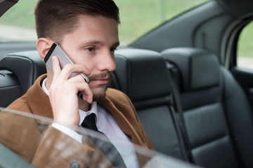 Portrait of a young business guy. Businessman rides in a car, in the passenger seat, talking on the phone, uses a smartphone