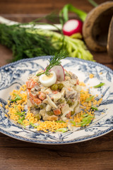 Traditional Russian salad Olivier with green pea and egg on wooden table