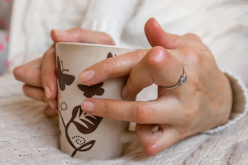 Young woman having rheumatoid arthritis is holding a cup of tea. Hands and legs are deformed. She...