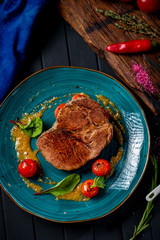 Large grilled beef steak on a plate with cherry tomatoes and mustard in plate on wooden dark...