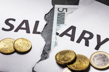 A sheet of white paper with the words salary torn in half with euro coins on the table