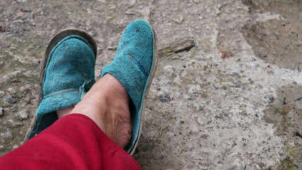 Female legs in old worn blue slippers on cement background. The concept of poverty, indifference,...