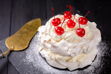 Pavlova cake with cocktail cherries on a dark background