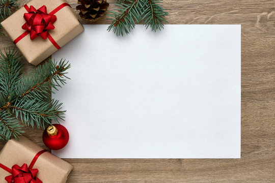 Christmas or New Year composition. White sheet of paper with copy space, gift boxes, Christmas ball and Christmas tree branches on wooden background. Flat lay, top view, horizontal layout