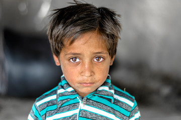 closeup of a poor staring hungry orphan boy in a refugee camp with sad expression on his face and...