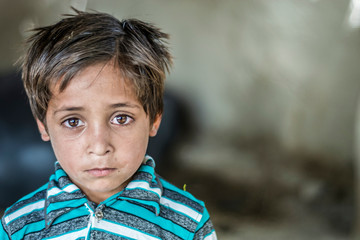 closeup of a poor staring hungry orphan boy in a refugee camp with sad expression on his face and...