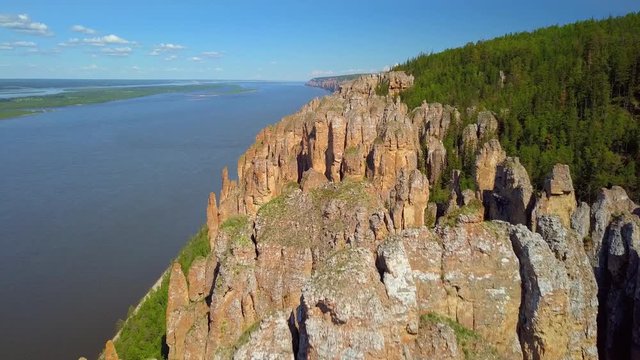 Aerial low forward Lena pillars tops of ancient rocks formation Russia blue widest river Lena channel beautiful landscape. Unique sight Yakutsk Sakha republic Summer blue sky clouds horizon open space