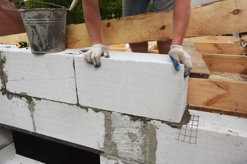 Bricklayer builder laying autoclaved aerated concrete blocks, aac for new house wall.