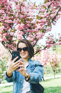 Young woman standing near cherry blossom tree and take Selfie