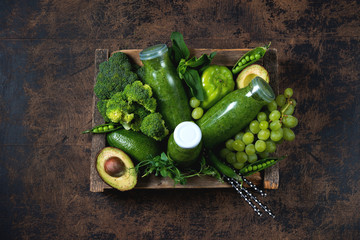 Three bottles of the healthiest green smoothie from vegetables and fruits are in a wooden box and around the green vegetables and fruits. Horizontal photo. Top view.