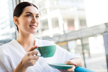 Portrait of attractive smiling woman in bathrobe drinking tea in wellness spa relaxation room after spa procedures