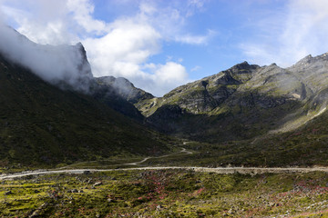 a small road in the blossoming valley, running between huge mountains covered with clouds. landscape from travel