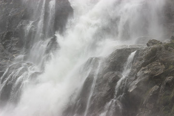 a huge stream of water falls on the rocks from a waterfall, throwing splashes of water