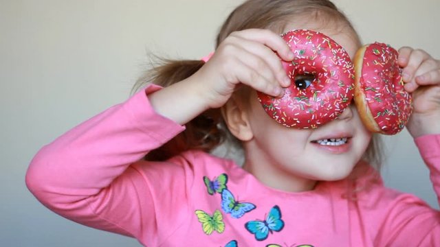 Child and donut. Closeup baby girl eating doughnut with glase. Delicious, sweet, sweettooth