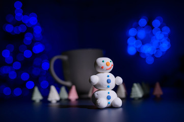 Cute snowman and little Christmas trees made of marshmallows on the background of Christmas lights....