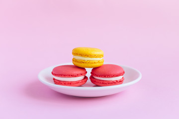 Three tasty french macarons on a white plate. Pink and yellow macarons. Pink background.