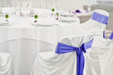 Beautiful wedding set decoration in the restaurant. Chairs with violet ribbons.