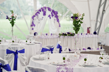 Beautiful wedding set decoration in the restaurant. Chairs with violet ribbons.