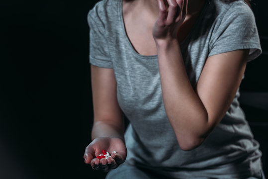 cropped view of depressed woman holding handful of pills and going to commit suicide isolated on black