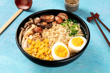 Ramen. Soba noodles with eggs, mushrooms, and vegetables, with sake, traditional wooden spoon, and chopsticks, on a blue background