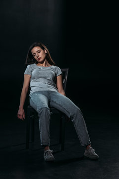 young, lifeless woman on chair after committing suicide on black background