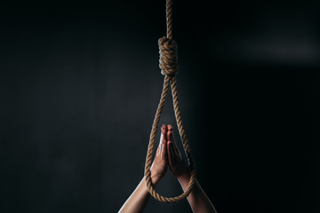 cropped of woman showing pray gesture near hanging rope noose on black background