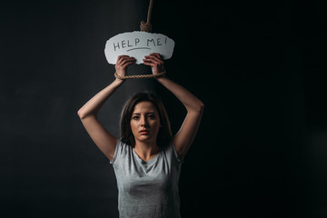 frustrated young woman holding paper with help me inscription while standing under hanging noose...