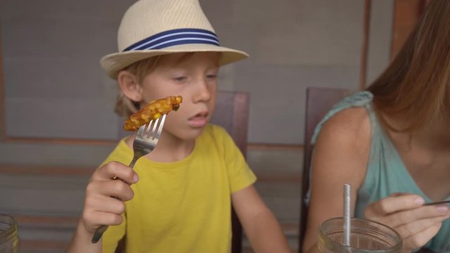 Young woman and her little son eat traditional Balenese food set Nasi Campur in a traditional cafe. Travel to Bali concept