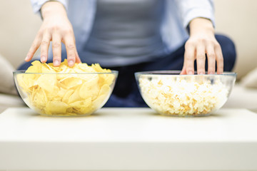 Obraz na płótnie Canvas Crop. Close up of unrecognizable woman grabbing popcorn and potato chips from large deep plates.