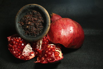 bowl with tobacco for hookah. red pomegranate on a black background. smoking nargile