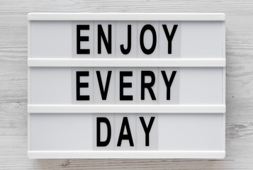 'Enjoy every day' words on a lightbox on a white wooden surface, top view. Overhead, from above, flat lay. Close-up.