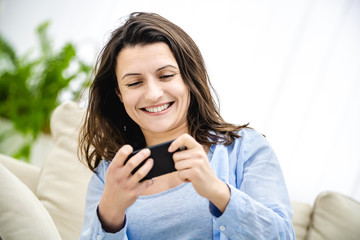 Attractive brunette woman is involved in phone game. She is smiling and trying to pass the level. Copy space. Close up.