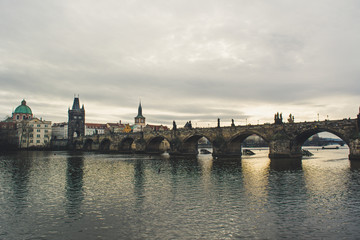 View of Charles Bridge on a couldy morning from riverbank with Vltava river in foreground, moody cold vibe 