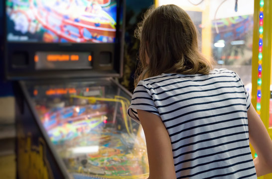 Little girl playing pinball game in theme park.