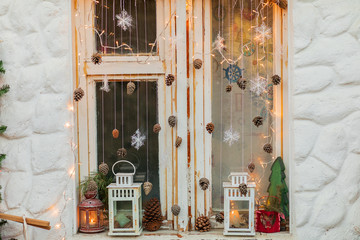 Christmas decor on an old window. Cones, snowflakes, candlestick, lanterns, candle, tree, deer, garland, retro, winter, new year, white wall.