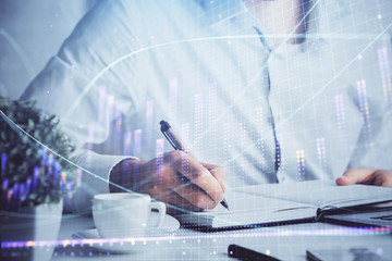 Double exposure of man's hands writing notes of stock market with forex chart.